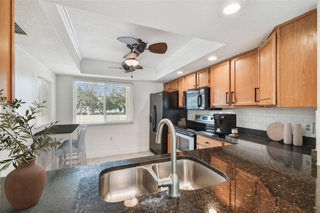 kitchen featuring a sink, dark stone counters, black appliances, tasteful backsplash, and a raised ceiling