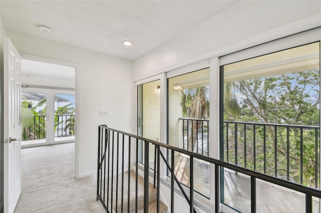 corridor with carpet floors, baseboards, a textured ceiling, and an upstairs landing