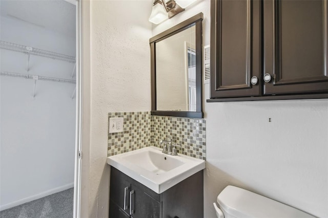 half bathroom with toilet, a textured wall, vanity, and decorative backsplash