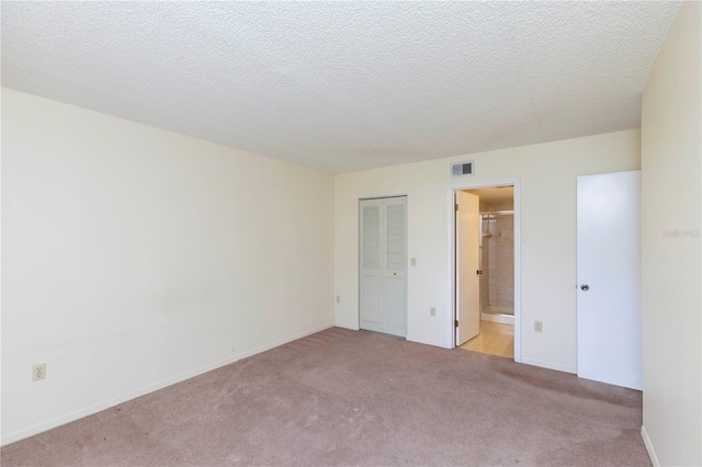 unfurnished bedroom with ensuite bathroom, light colored carpet, a textured ceiling, and a closet