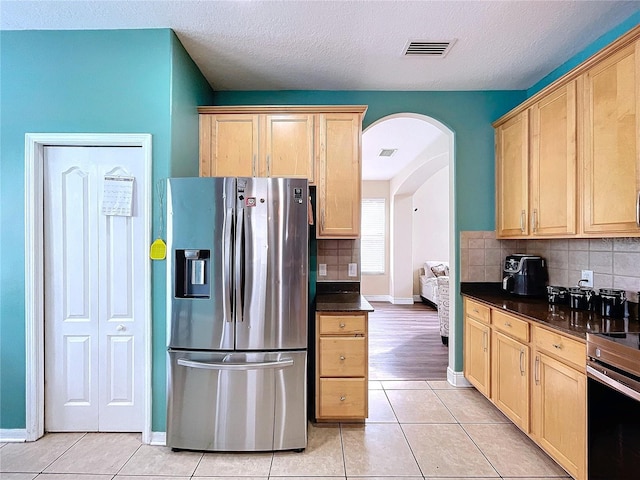 kitchen with light tile patterned floors, a textured ceiling, light brown cabinetry, tasteful backsplash, and stainless steel appliances