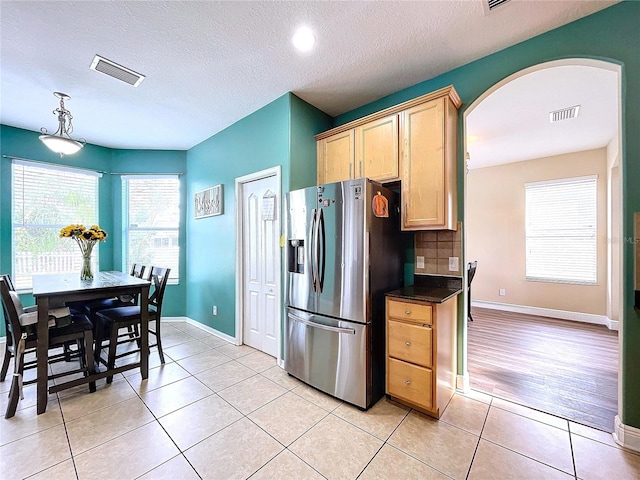 kitchen featuring backsplash, a textured ceiling, light brown cabinetry, light tile patterned flooring, and stainless steel fridge with ice dispenser