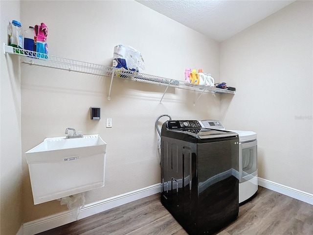 clothes washing area with washing machine and clothes dryer, sink, a textured ceiling, and hardwood / wood-style flooring