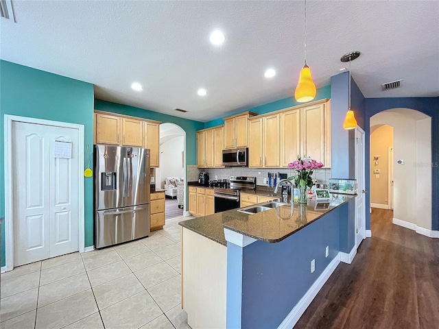 kitchen with sink, light brown cabinets, kitchen peninsula, pendant lighting, and appliances with stainless steel finishes