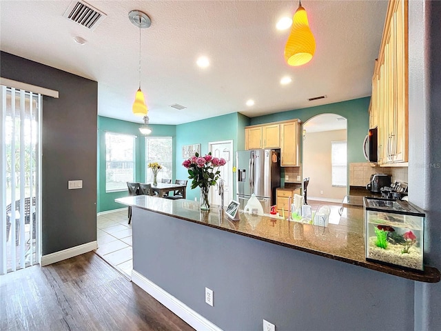 kitchen with backsplash, kitchen peninsula, dark stone counters, decorative light fixtures, and appliances with stainless steel finishes