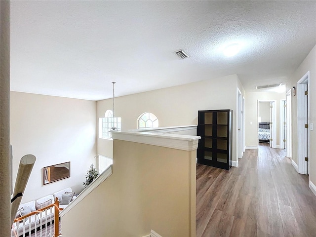 hallway with hardwood / wood-style flooring, a textured ceiling, and a chandelier