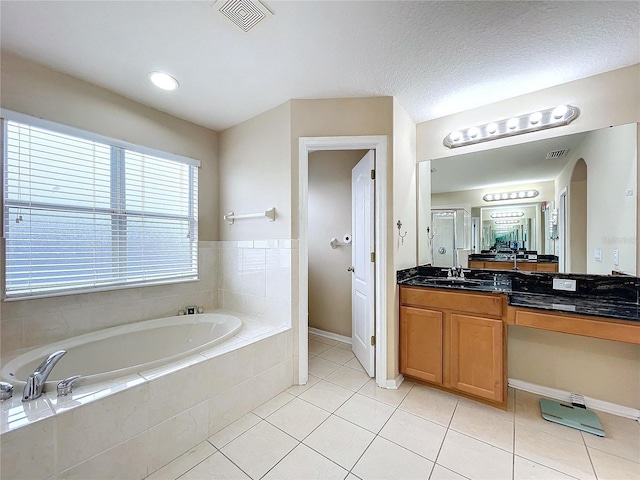 bathroom featuring tile patterned floors, vanity, a textured ceiling, and tiled tub