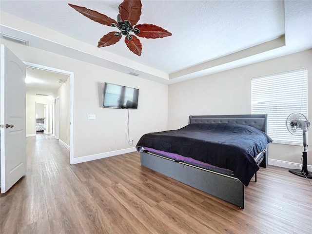 bedroom with wood-type flooring, a textured ceiling, a raised ceiling, and ceiling fan