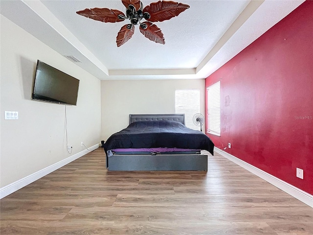 bedroom featuring a textured ceiling, a tray ceiling, light hardwood / wood-style flooring, and ceiling fan