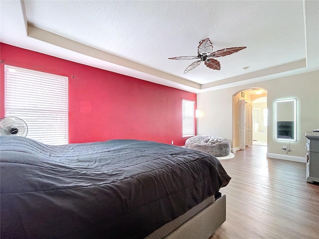 bedroom featuring a tray ceiling, ceiling fan, a textured ceiling, and hardwood / wood-style flooring