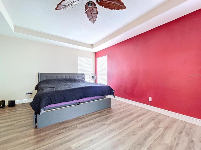 bedroom featuring a tray ceiling, light hardwood / wood-style flooring, and a textured ceiling