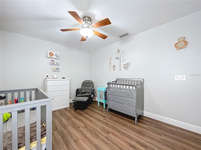 bedroom featuring a textured ceiling, dark hardwood / wood-style floors, a nursery area, and ceiling fan