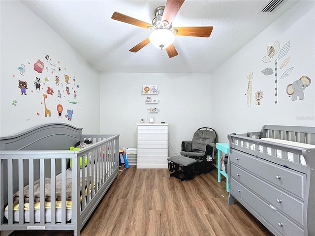 bedroom with a crib, a textured ceiling, hardwood / wood-style flooring, and ceiling fan