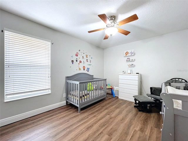 bedroom with hardwood / wood-style flooring, ceiling fan, a crib, and multiple windows