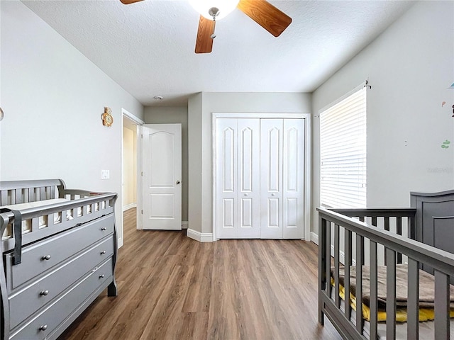 bedroom with hardwood / wood-style floors, ceiling fan, a crib, and a closet