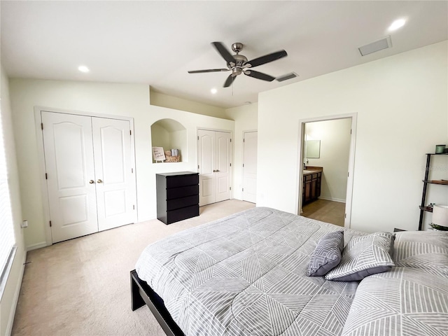 carpeted bedroom with ensuite bath, ceiling fan, and two closets