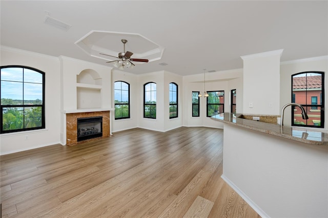 unfurnished living room featuring a tile fireplace, ceiling fan, light hardwood / wood-style flooring, crown molding, and a tray ceiling