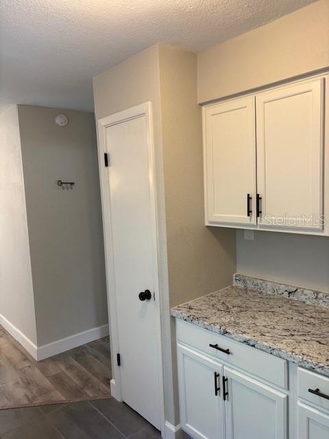 kitchen featuring light stone countertops, a textured ceiling, dark hardwood / wood-style flooring, and white cabinetry