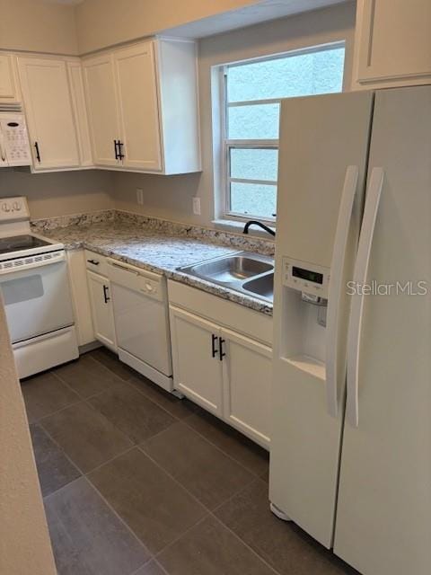 kitchen with white cabinetry, sink, dark tile patterned floors, and white appliances