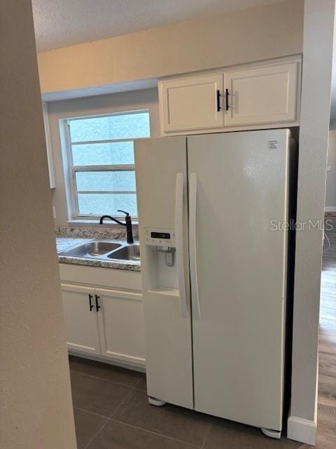 kitchen featuring dark tile patterned flooring, white cabinetry, white fridge with ice dispenser, and sink