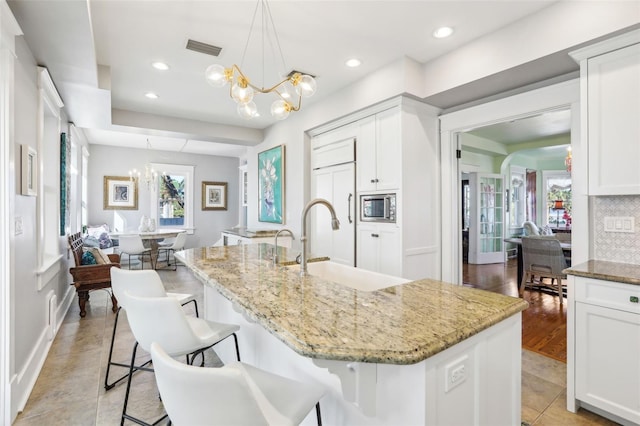 kitchen with tasteful backsplash, an island with sink, stainless steel microwave, and an inviting chandelier