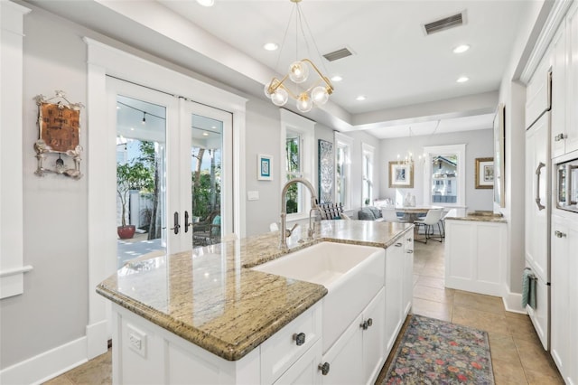 kitchen featuring decorative light fixtures, sink, white cabinets, a kitchen island with sink, and french doors