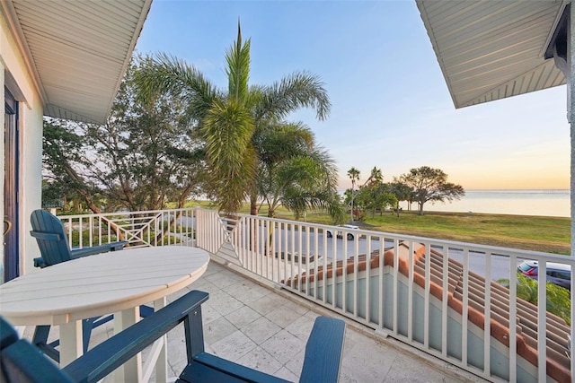 balcony at dusk featuring a water view