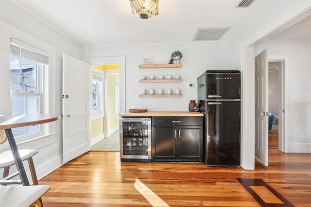 bar with beverage cooler, light hardwood / wood-style floors, crown molding, black fridge, and a textured ceiling