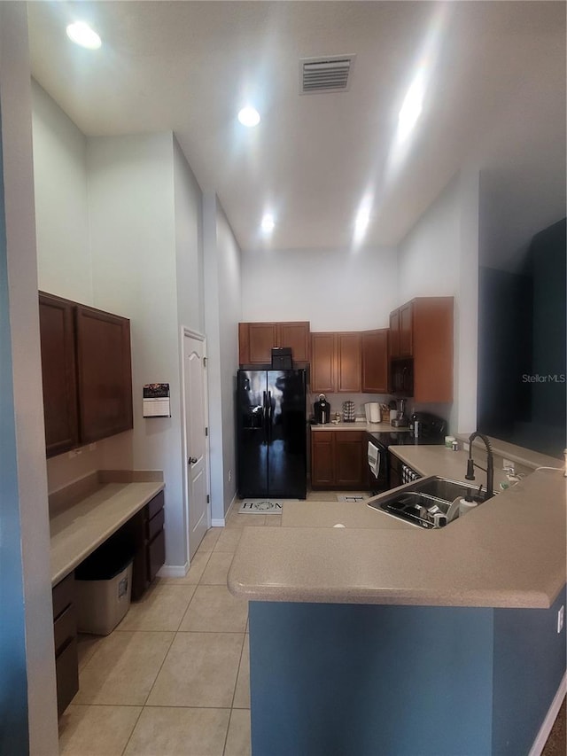 kitchen with a high ceiling, black fridge, sink, light tile patterned floors, and kitchen peninsula