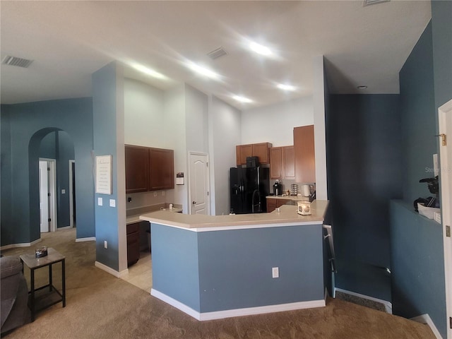 kitchen with kitchen peninsula, a high ceiling, light colored carpet, and black refrigerator with ice dispenser