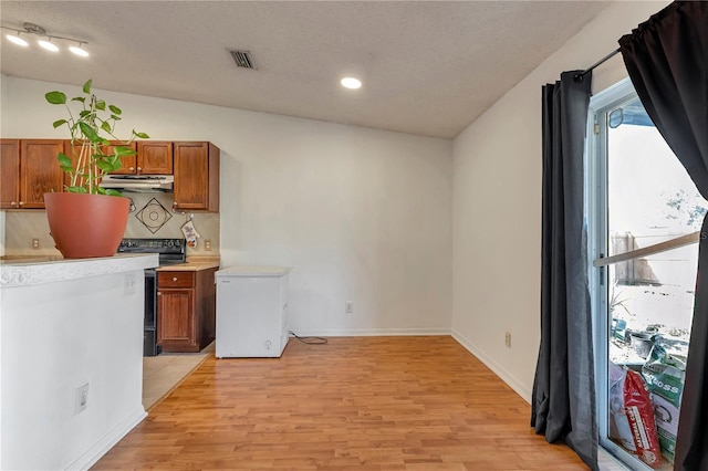 kitchen featuring black electric range oven, backsplash, a textured ceiling, fridge, and light wood-type flooring