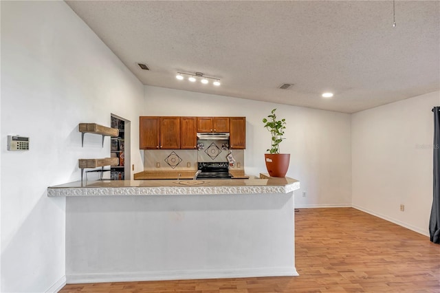 kitchen with light wood-type flooring, kitchen peninsula, a textured ceiling, and tasteful backsplash