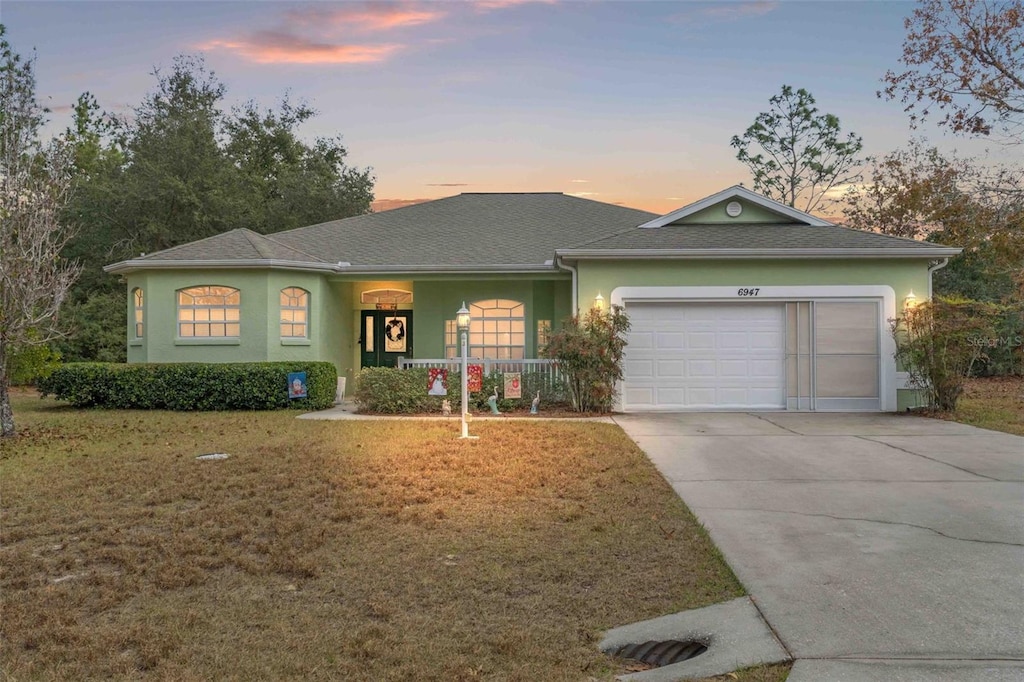 single story home with a lawn, covered porch, and a garage