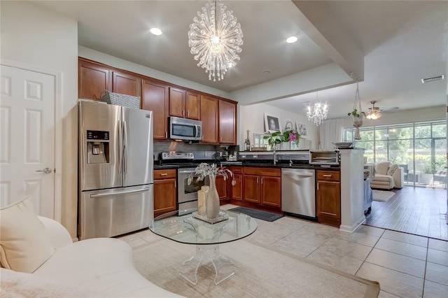 kitchen with tasteful backsplash, decorative light fixtures, light tile patterned floors, ceiling fan with notable chandelier, and appliances with stainless steel finishes