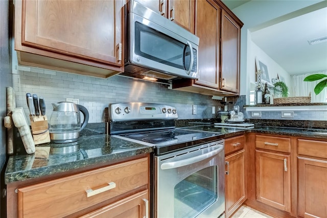 kitchen with backsplash, stainless steel appliances, and dark stone counters