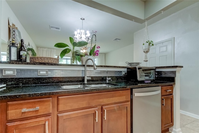 kitchen with dark stone counters, sink, light tile patterned floors, dishwasher, and a chandelier