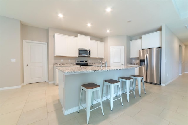 kitchen featuring light stone countertops, stainless steel appliances, white cabinetry, and a center island with sink