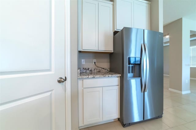 kitchen with stainless steel fridge, light tile patterned floors, white cabinetry, and light stone counters