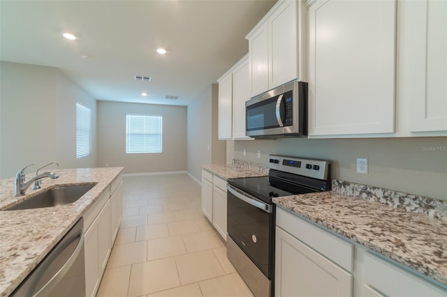 kitchen with light stone counters, stainless steel appliances, white cabinetry, and sink