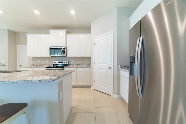 kitchen with white cabinets, appliances with stainless steel finishes, light stone counters, and sink