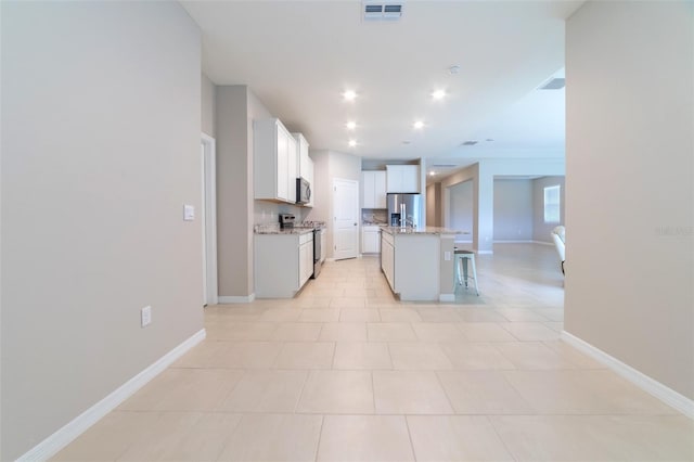 kitchen featuring light stone countertops, an island with sink, a kitchen bar, white cabinets, and appliances with stainless steel finishes