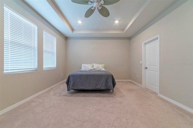 bedroom featuring ceiling fan, a raised ceiling, light colored carpet, and multiple windows