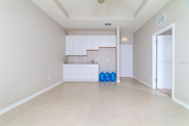 kitchen featuring white cabinets, light tile patterned flooring, light stone counters, and a tray ceiling