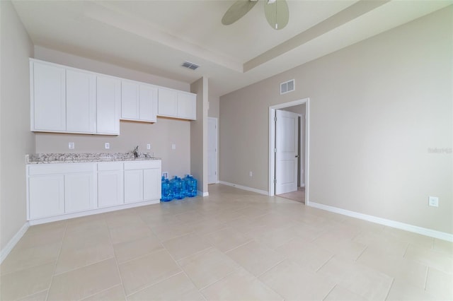 kitchen with sink, ceiling fan, light tile patterned floors, light stone counters, and white cabinetry