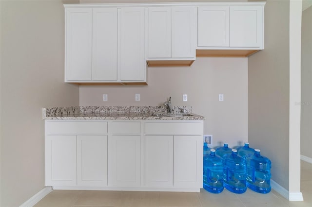 kitchen featuring light stone countertops, light tile patterned floors, white cabinetry, and sink