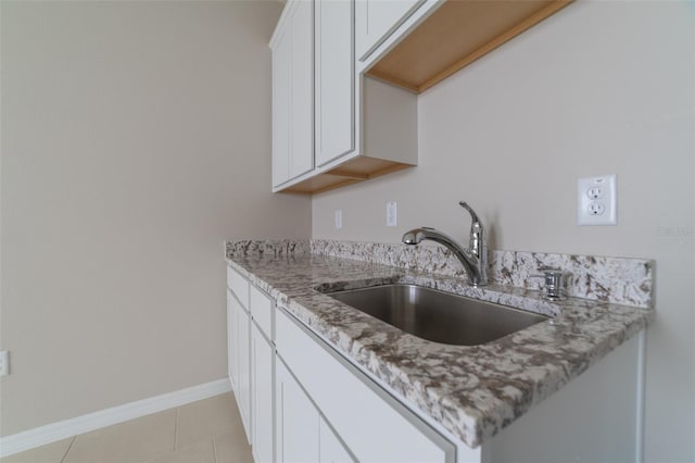 kitchen featuring white cabinets, light tile patterned floors, light stone counters, and sink