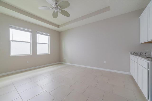 tiled empty room featuring a tray ceiling and ceiling fan