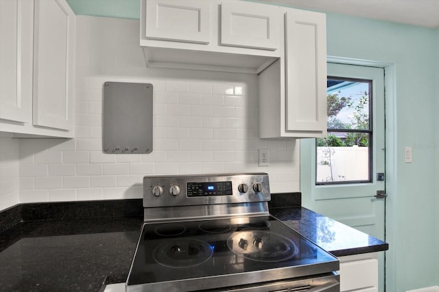 kitchen featuring white cabinets, decorative backsplash, stainless steel range with electric stovetop, and dark stone countertops