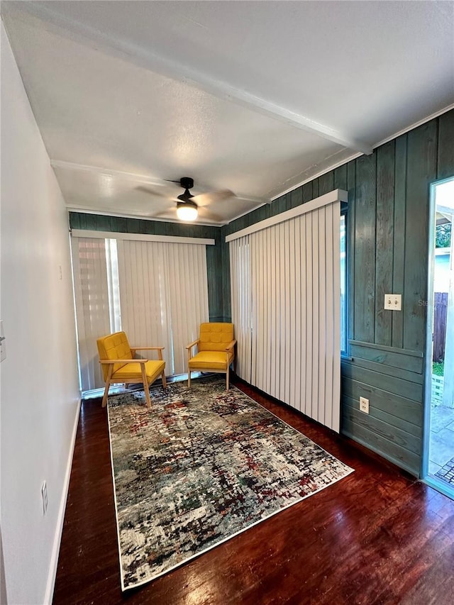 living area with ceiling fan, wood walls, and dark wood-type flooring