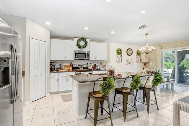 kitchen with a breakfast bar, appliances with stainless steel finishes, white cabinetry, and dark stone countertops